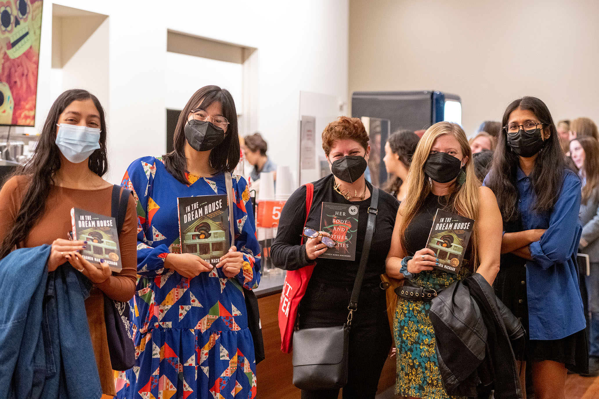 5 women wearing black face masks stand in front of the camera smiling. 3 women are holding the book "In the Dream House" and one is holding the book "Her Body and Other Parties".
